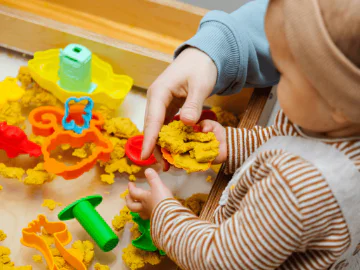 Baby playing in a sensory sandpit with parent