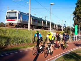 Cyclists riding along a shared path, next to a train line with a train heading towards Midland