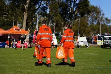 Two SES staff walk across an oval in an orange SES uniform.