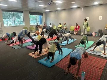 A group of people of all ages doing a yoga pose in a room on yoga mats
