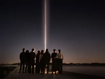 People gathered by a river looking at a beam of light