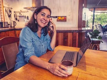 A woman at home working on a laptop while on the phone