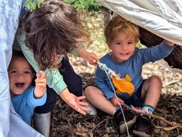 Three children playing in a pile of leaves in a park