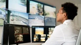 A man sits at screens showing footage from security cameras