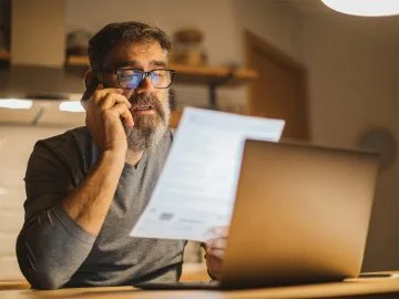 A man on the phone, holding a printed form in his hand at a computer