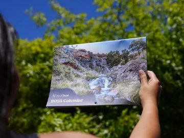 Woman hold new community calendar in front of a green tree