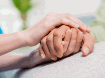 A young person holding an older person's hand in a caring manner.